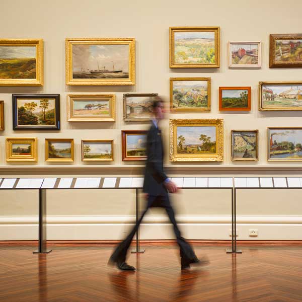 A man strolls past a wall adorned with various paintings in an art gallery