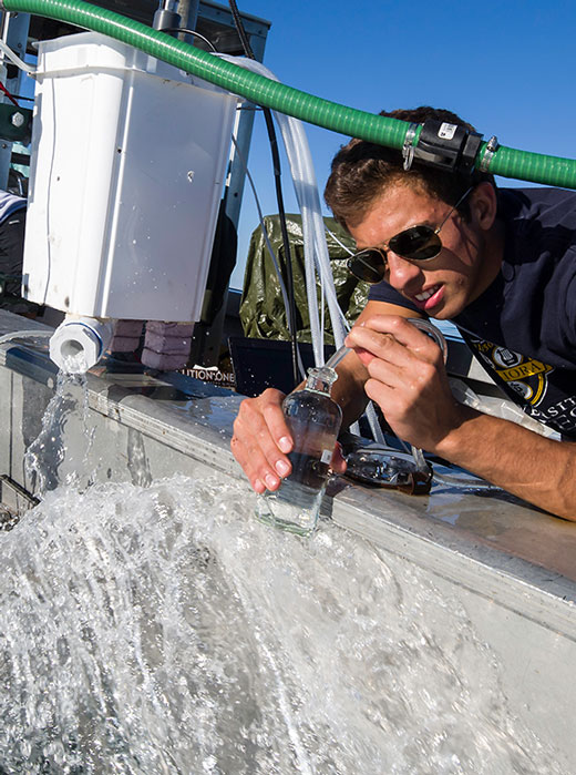 A University of Rochester student in a boat holds a bottle while conducting research in the field.