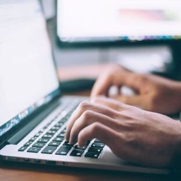 A person focused on typing on a laptop computer, with hands positioned on the keyboard and a screen visible.
