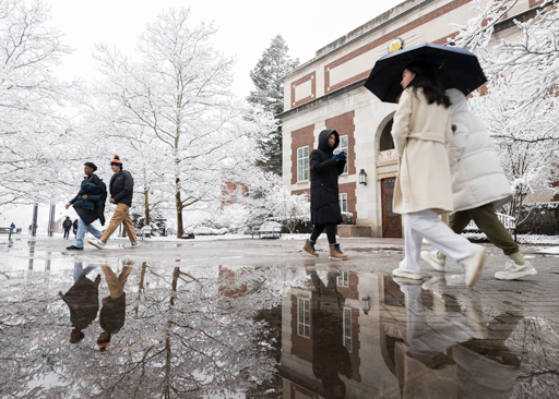Students walking on a snowy sidewalk at the University of Rochester's river campus during winter weather.