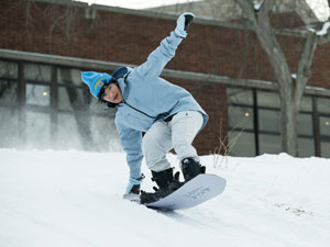 A University of Rochester student expertly rides a snowboard down a snowy slope, capturing the thrill of winter fun.