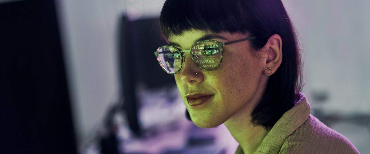 A woman with glasses focused on her computer screen, engaged in work or study.