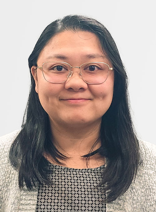 A woman wearing glasses and a cozy sweater smiles warmly, radiating joy and positivity.