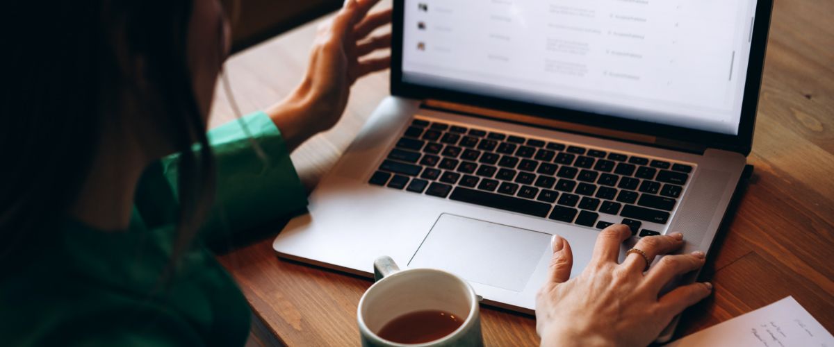 Person using a laptop at a wooden desk with a coffee mug nearby.